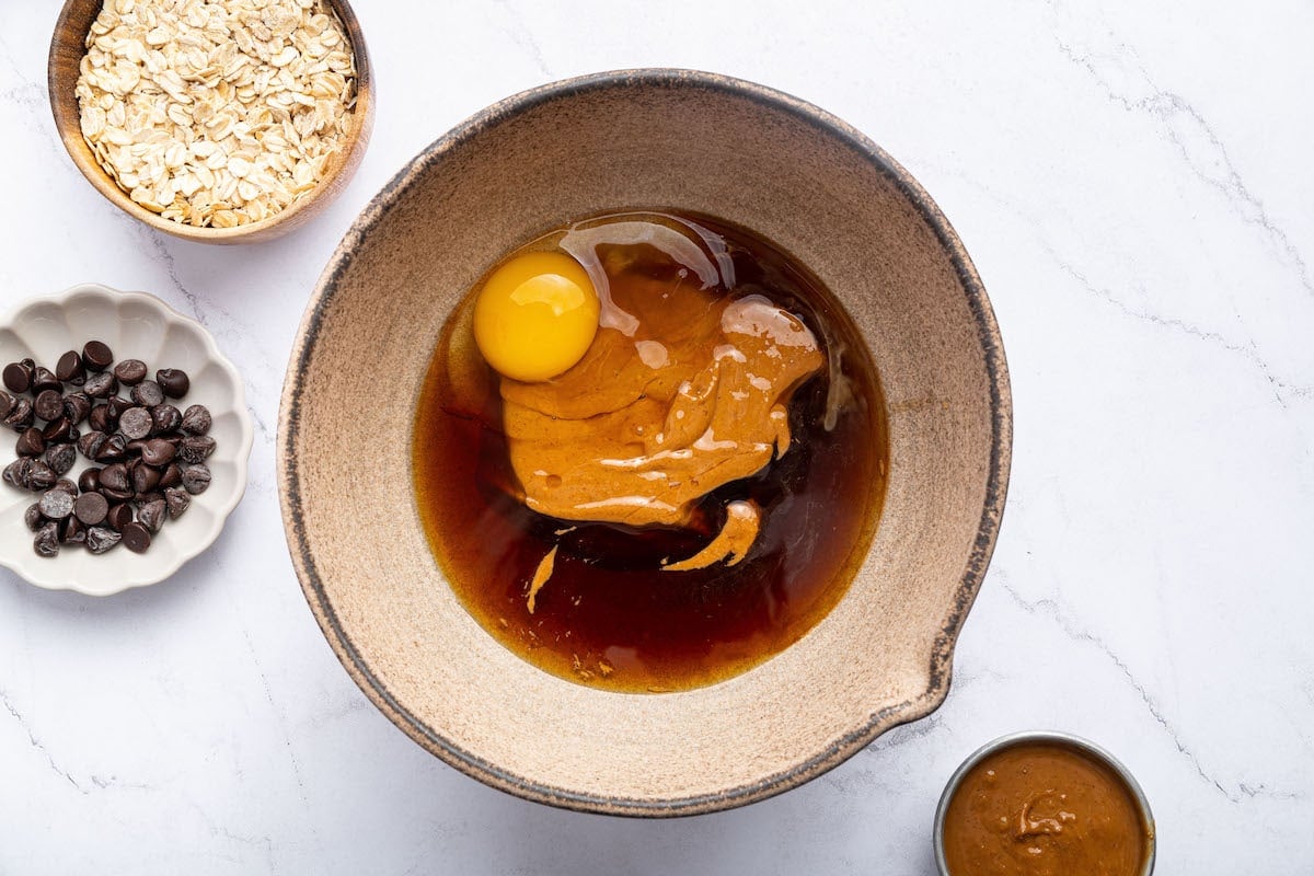 Wet ingredients, including peanut butter, egg, and maple syrup in a large mixing bowl.
