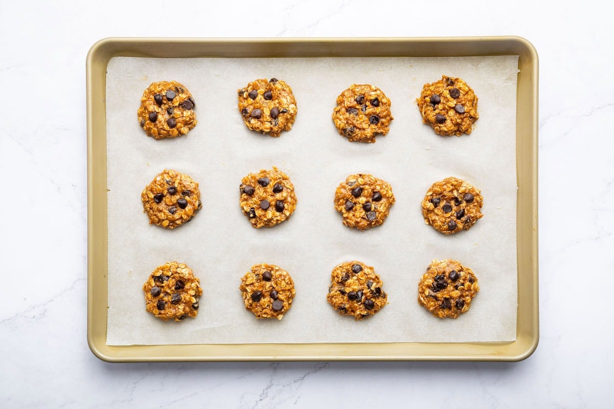 Twelve peanut butter oatmeal cookies on a baking tray before being baked.