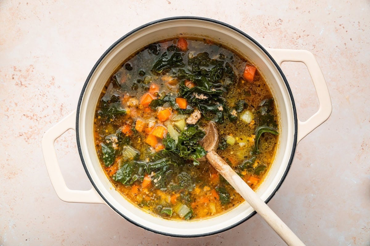 A pot of sausage and kale soup served with a wooden spoon.