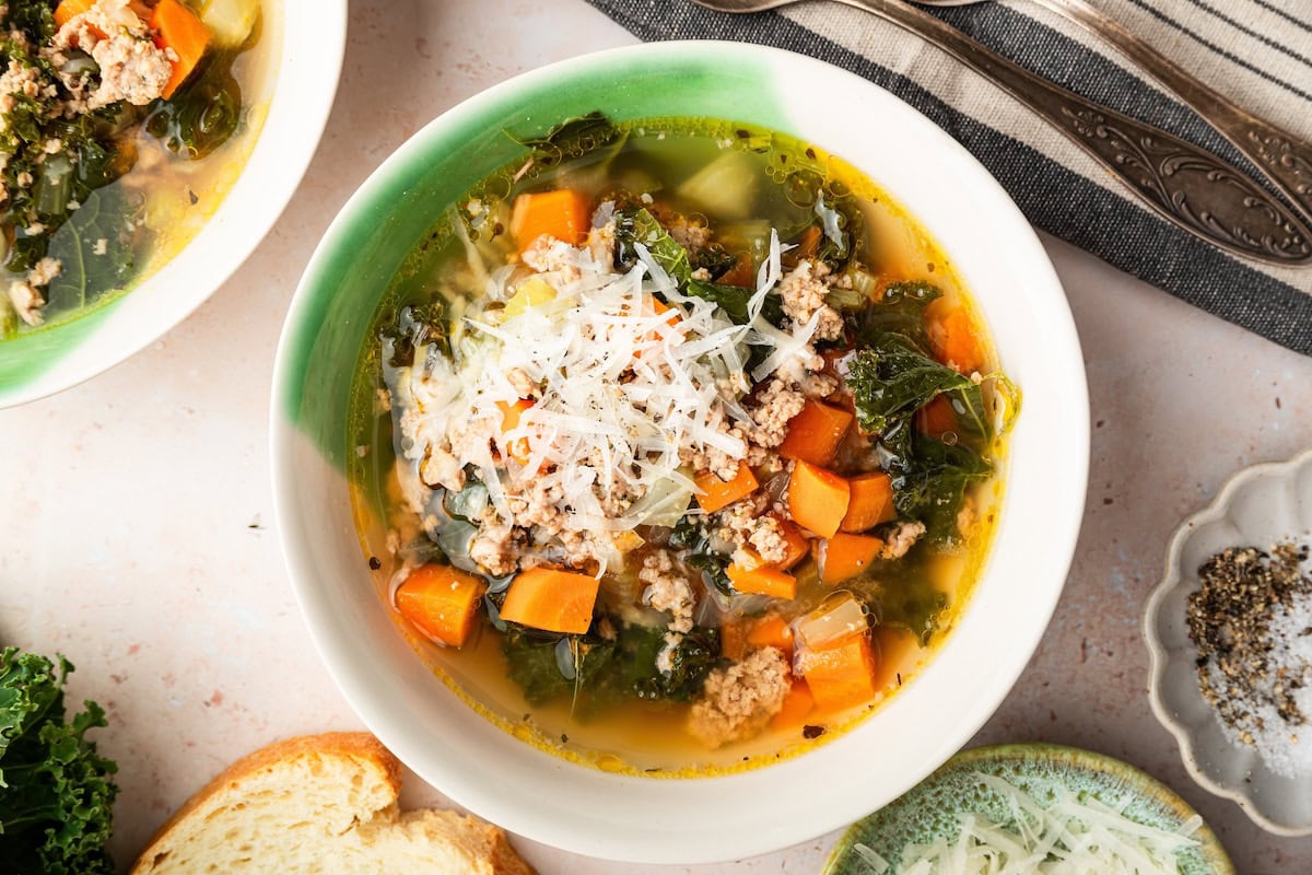 Sausage and kale soup served up in a green and white soup bowl. The soup is topped with grated parmesan cheese.