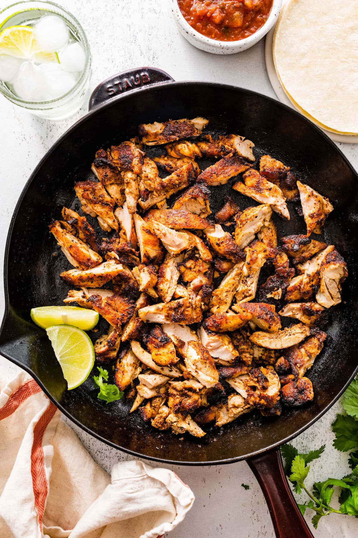 Sliced chipotle chicken cooked in a cast iron skillet. There are two lime wedges in the skillet next to the chicken.