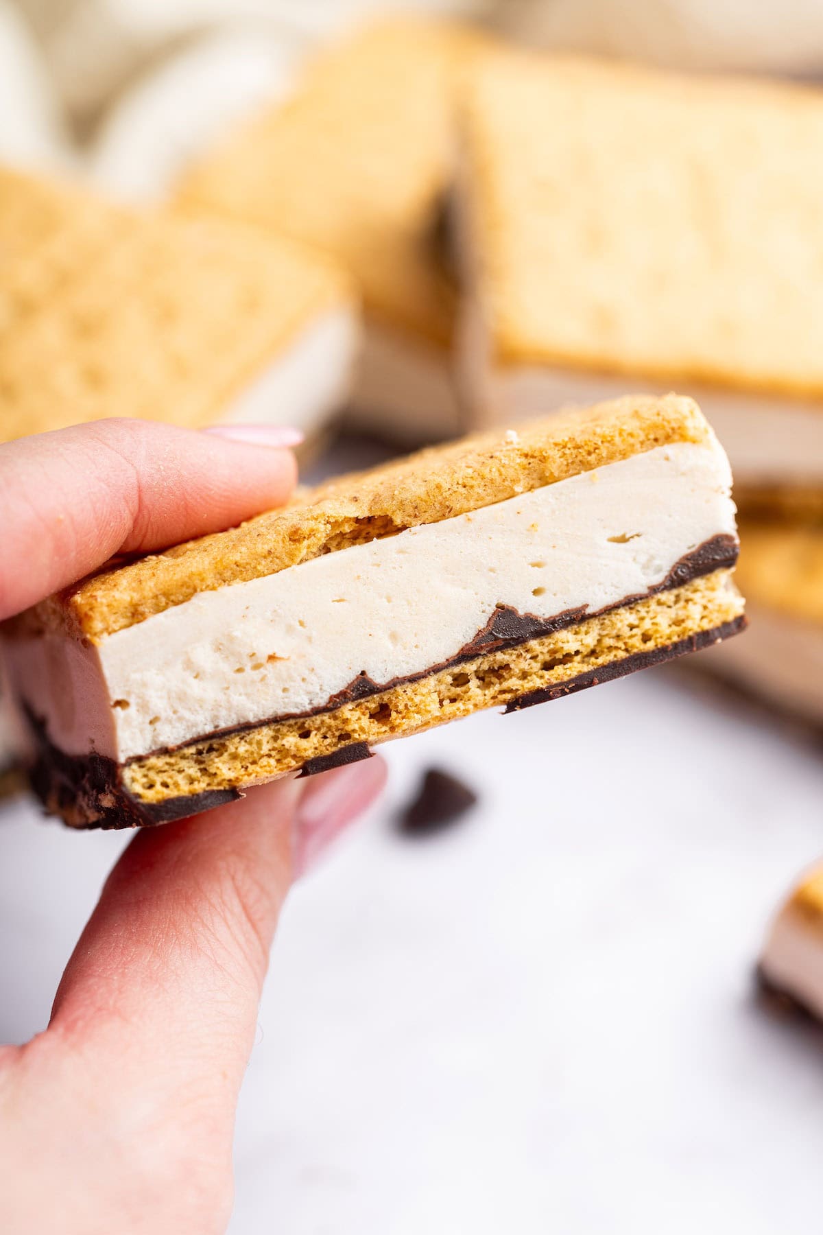 Hand holding a single frozen s’mores bar showing chocolate and creamy protein layer.