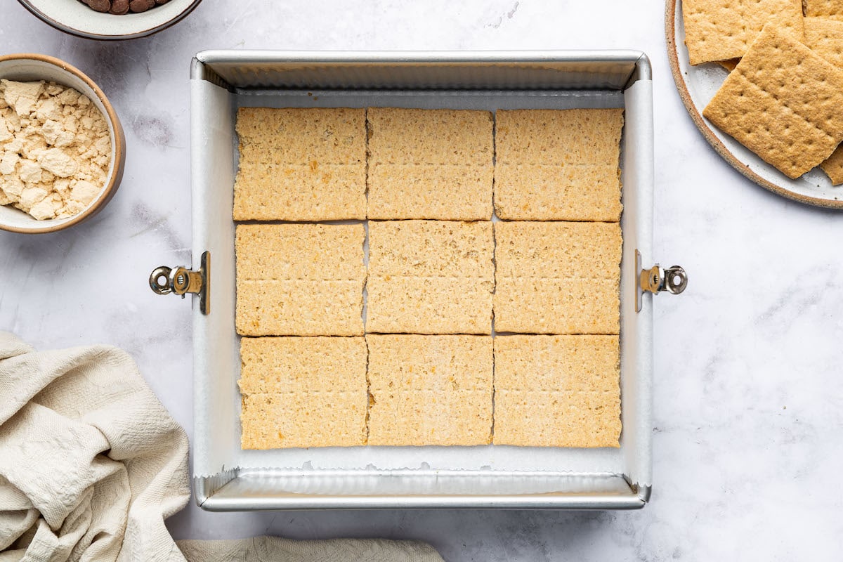 Frozen s’mores bars cut into squares and arranged in a metal pan lined with parchment paper.