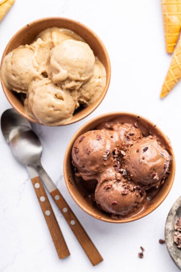 Two bowls of protein ice cream-one is chocolate and one is vanilla. There are two spoons next to the bowls.