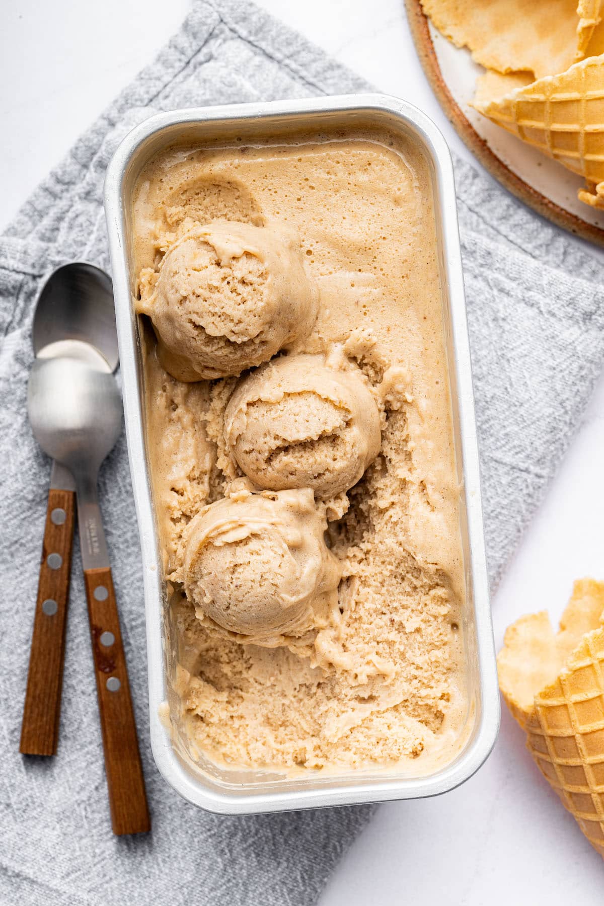 Vanilla protein ice cream in a loaf pan with three scoops of the ice cream. There are two spoons next to the ice cream.