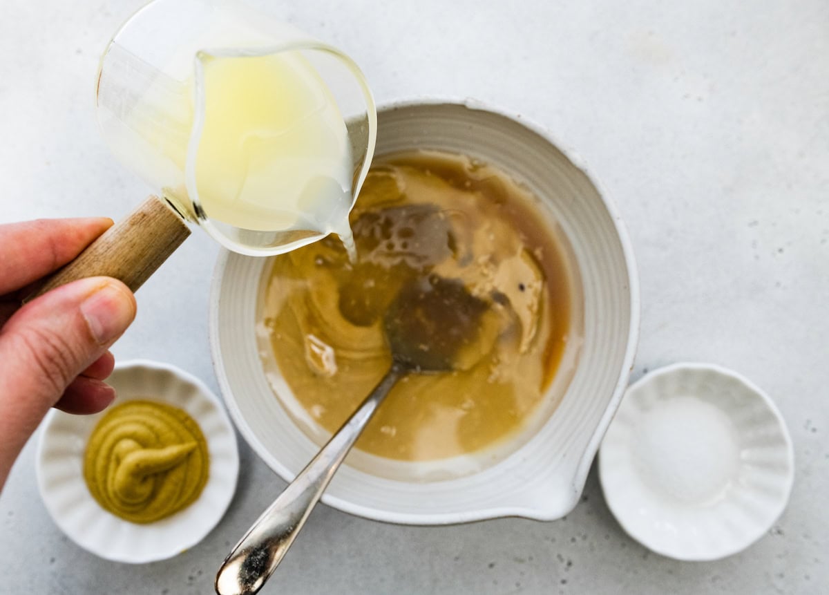 Lemon juice is being poured into a bowl of more ingredients to make a tahini dressing.