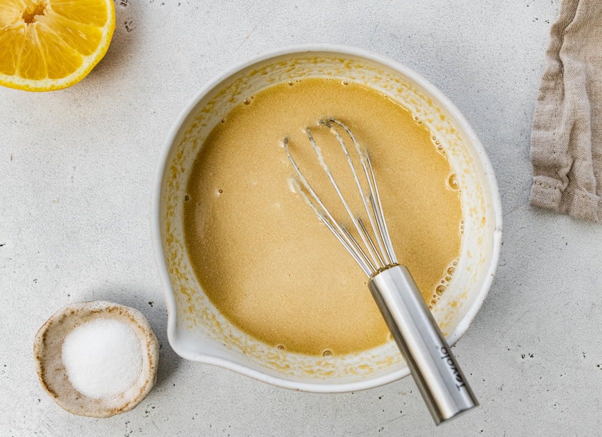 A tahini dressing in a bowl with a metal whisk.