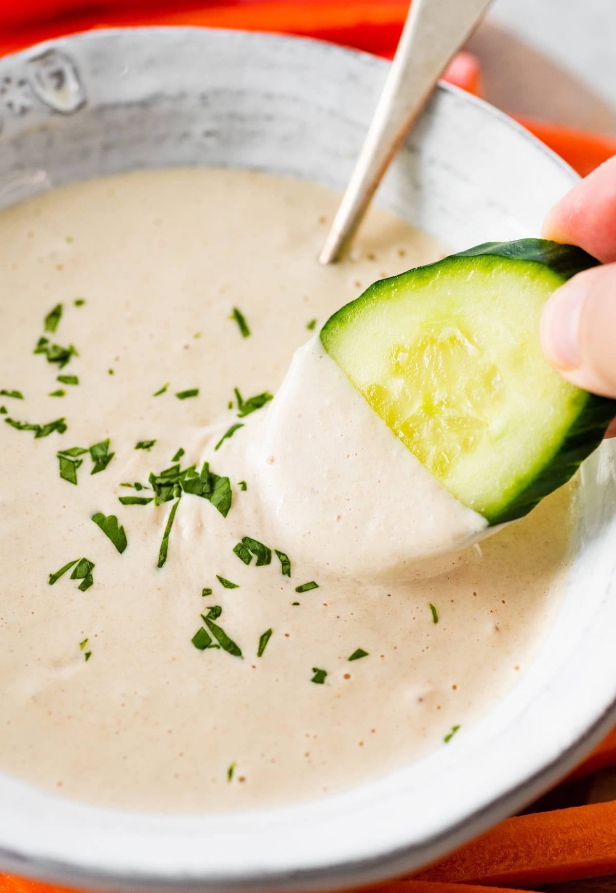 A cucumber slice being dipping into a bowl filled with tahini sauce.