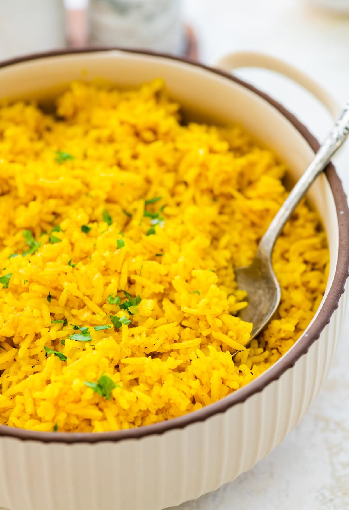 A pot of cooked turmeric rice topped with fresh parsley. There is a silver spoon in the rice.