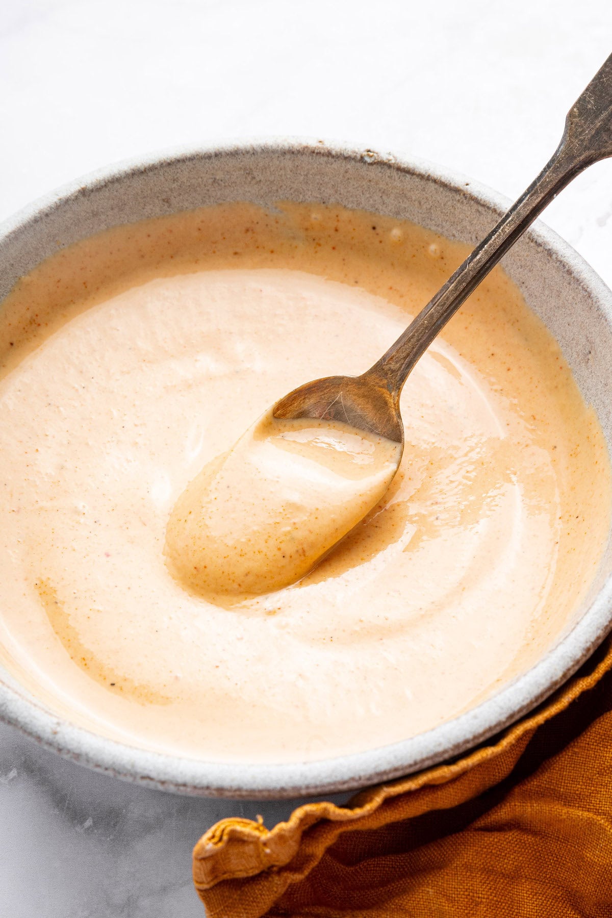 Easy yum yum sauce in a small ceramic bowl with a silver spoon scooping up some of the sauce.