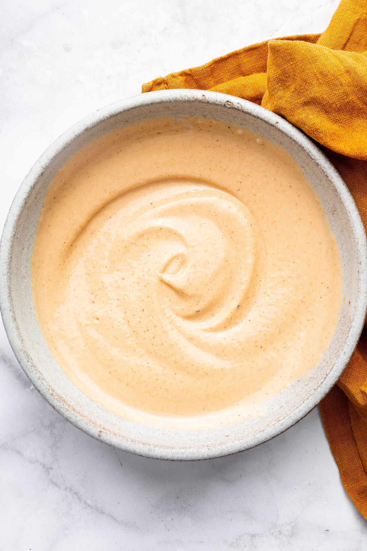 Easy yum yum sauce in a small ceramic bowl. There is an orange linen towel next to the bowl.