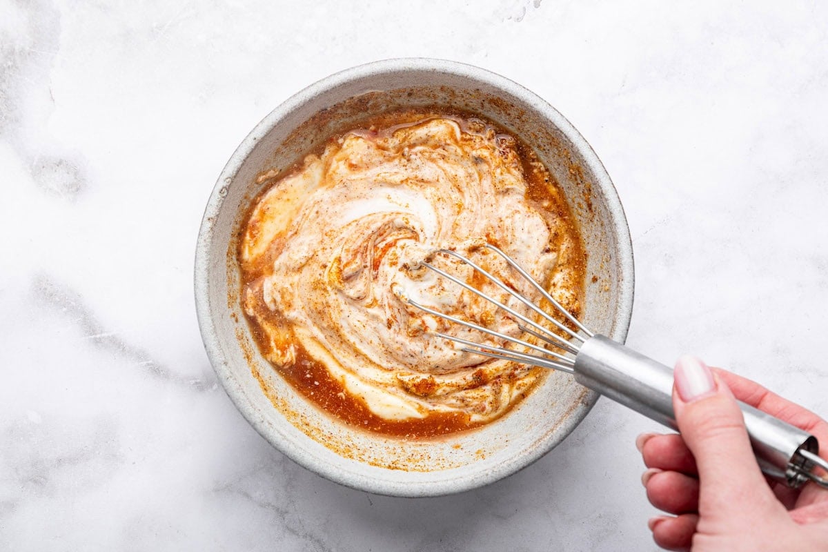 A woman's hand whisking together the yum yum sauce in a small ceramic bowl.
