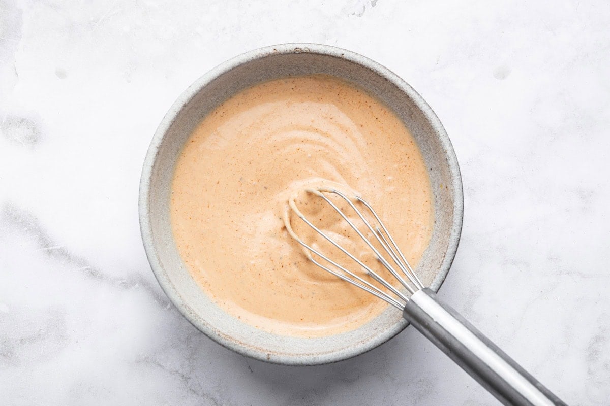 A silver whisk mixing together the homemade yum yum sauce recipe in a small ceramic bowl.