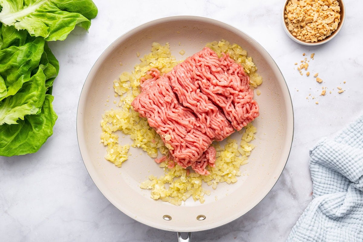 Raw ground chicken added to a skillet with sautéed onion and garlic.