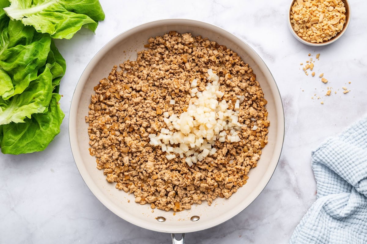 Water chestnuts added to the ground chicken mixture in a skillet.