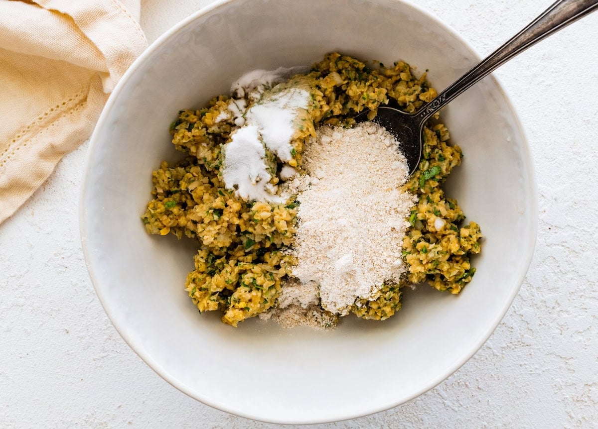 Falafel mixture in bowl with oat flour and baking soda being added.