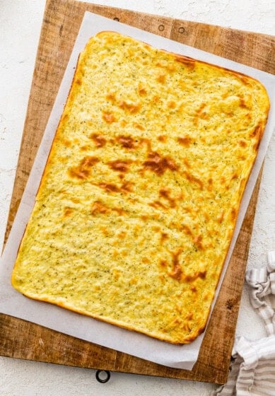 A baked cottage cheese flatbread on parchment paper on top of a wooden cutting board.