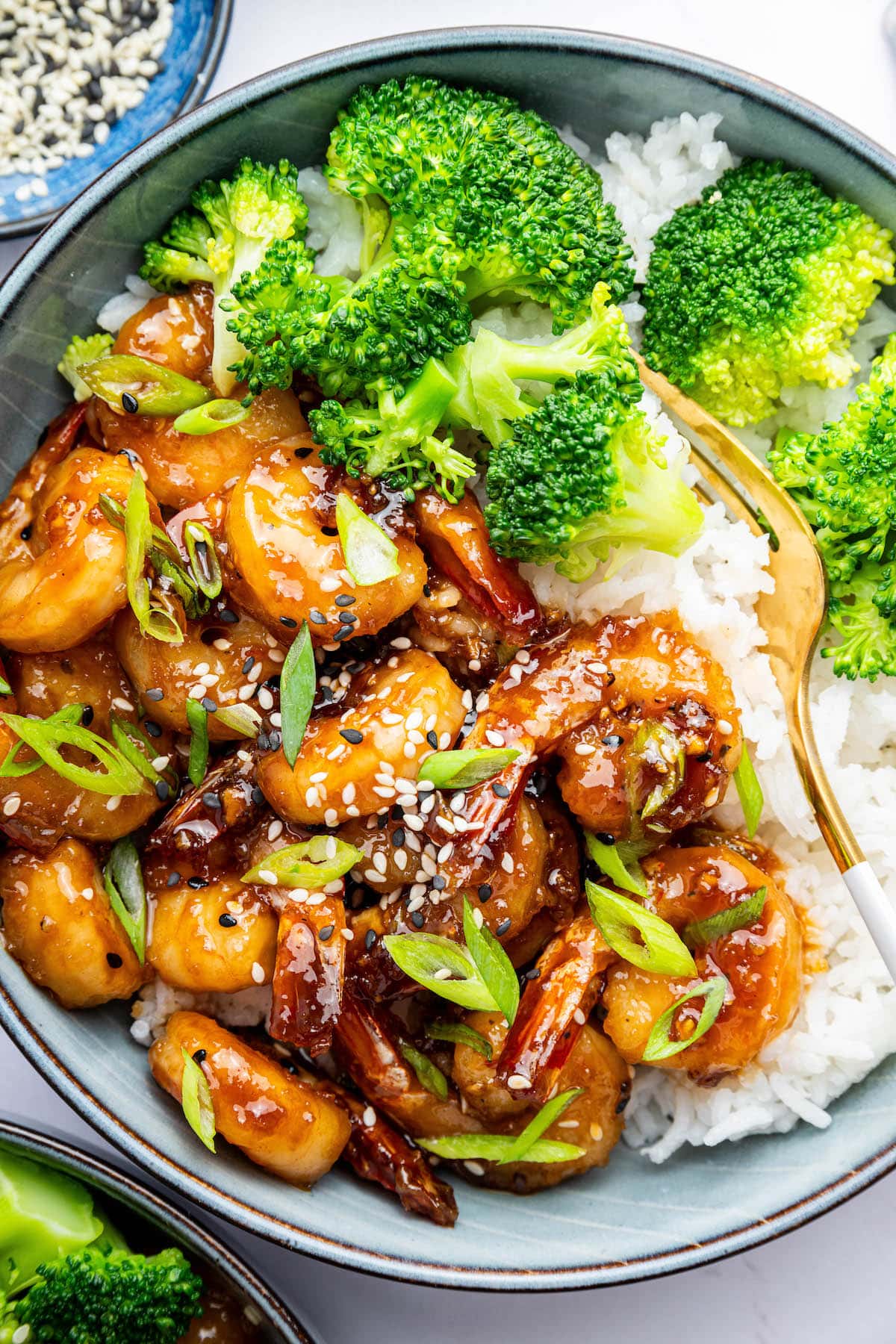 Honey garlic shrimp served in a blue bowl with white rice and steamed broccoli. The shrimp is topped with sesame seeds and green onion slices.