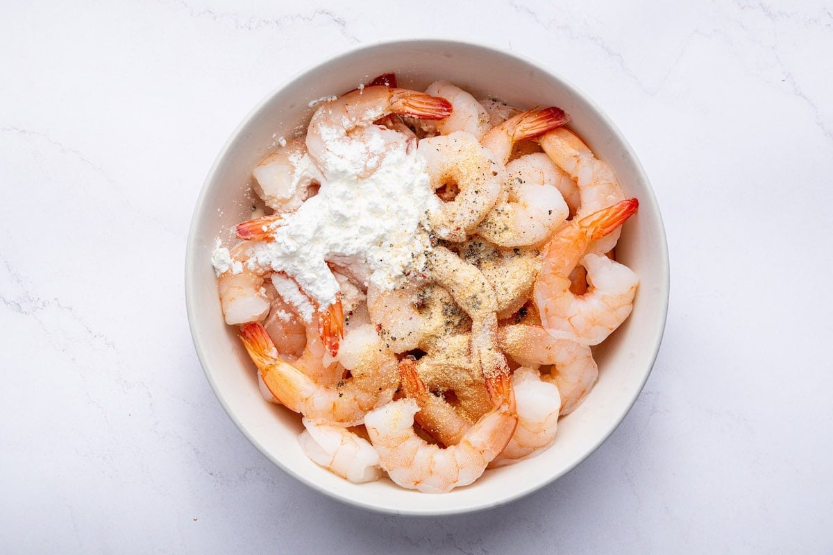Raw shrimp in a bowl tossed with arrowroot powder, garlic powder, salt and pepper.