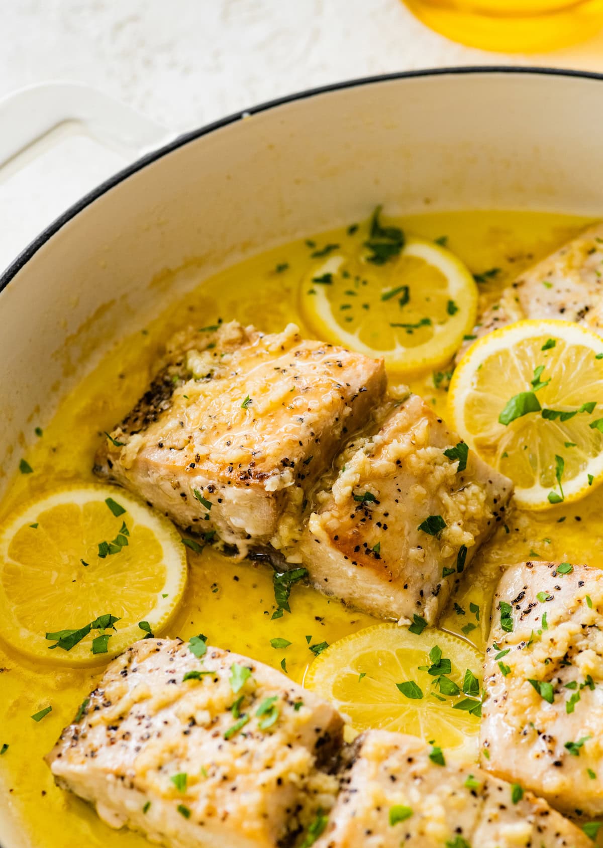 Mahi mahi fillets in a skillet with a lemon butter garlic sauce. There are lemon slices in the skillet and everything is topped with fresh parsley.