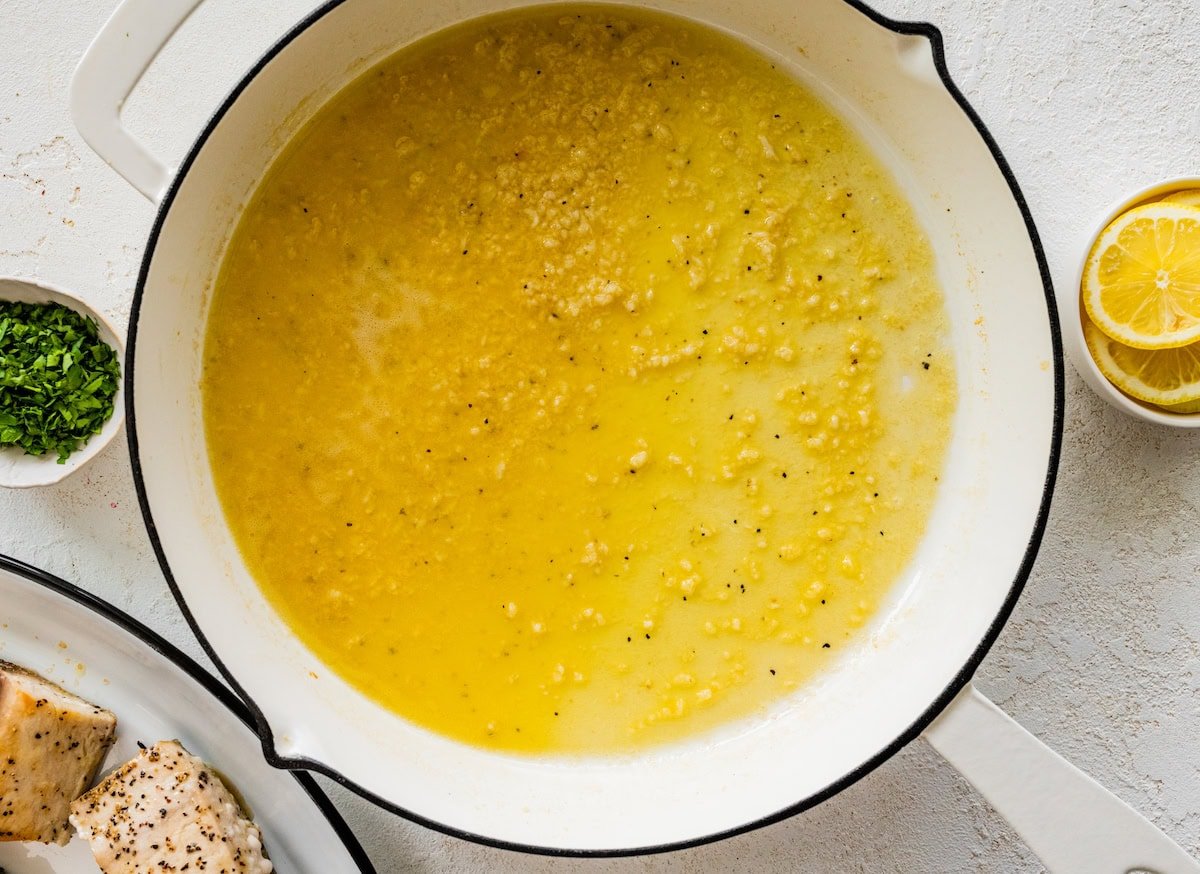 The lemon butter garlic sauce for the mahi mahi cooking in a white skillet.