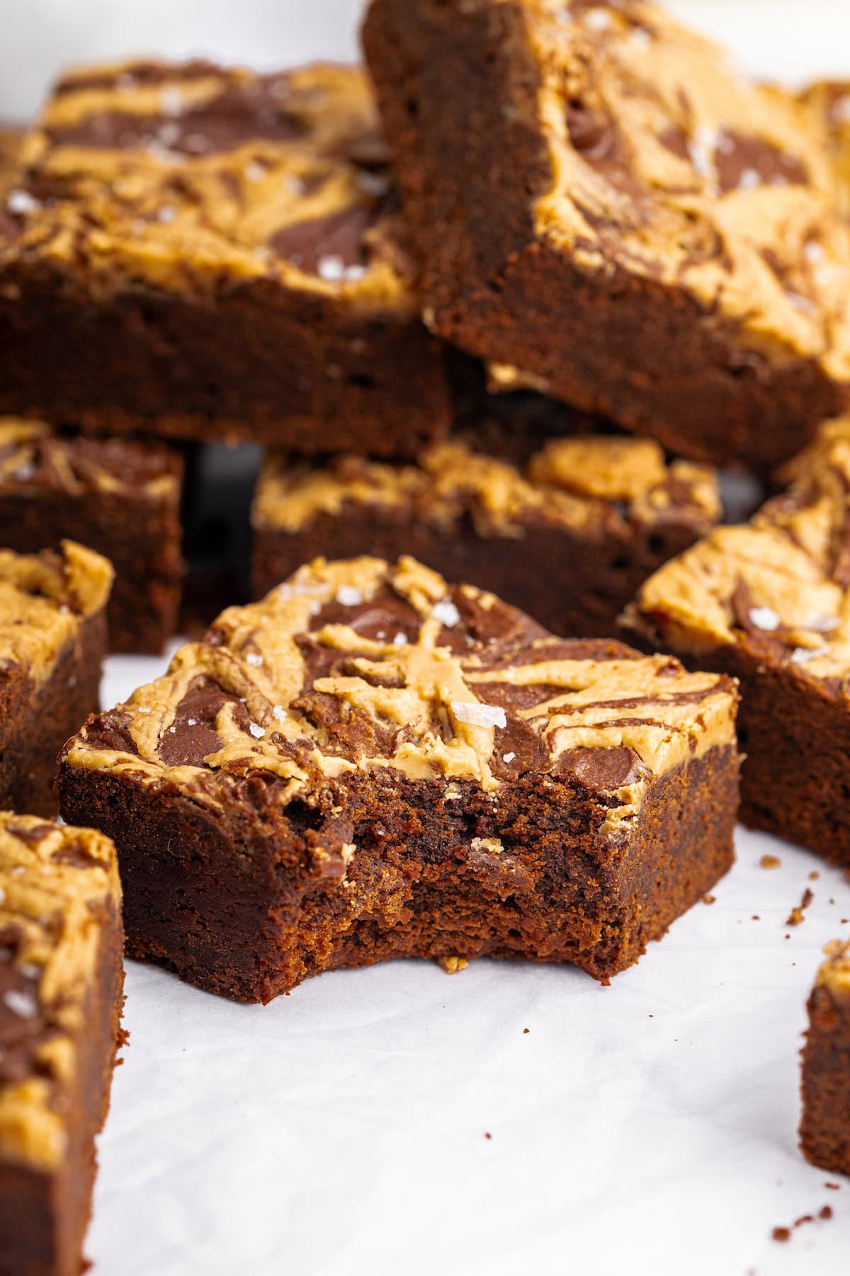 One peanut butter brownie with a bite taken out of it. Multiple peanut butter brownies are in the background stacked on top of each other.