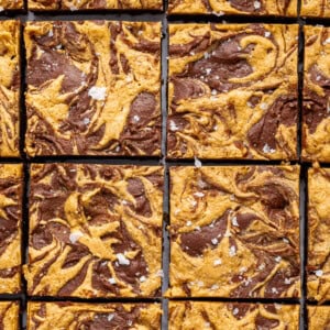 Peanut butter brownies cut into 16 squares. The brownies are topped with a peanut butter swirl and flaked sea salt.