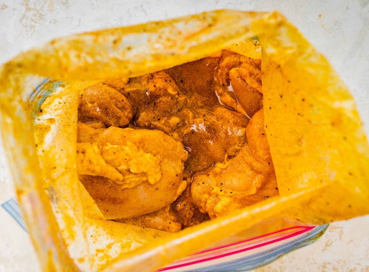 A large ziplock bag of chicken thighs marinating in multiple herbs and spices.