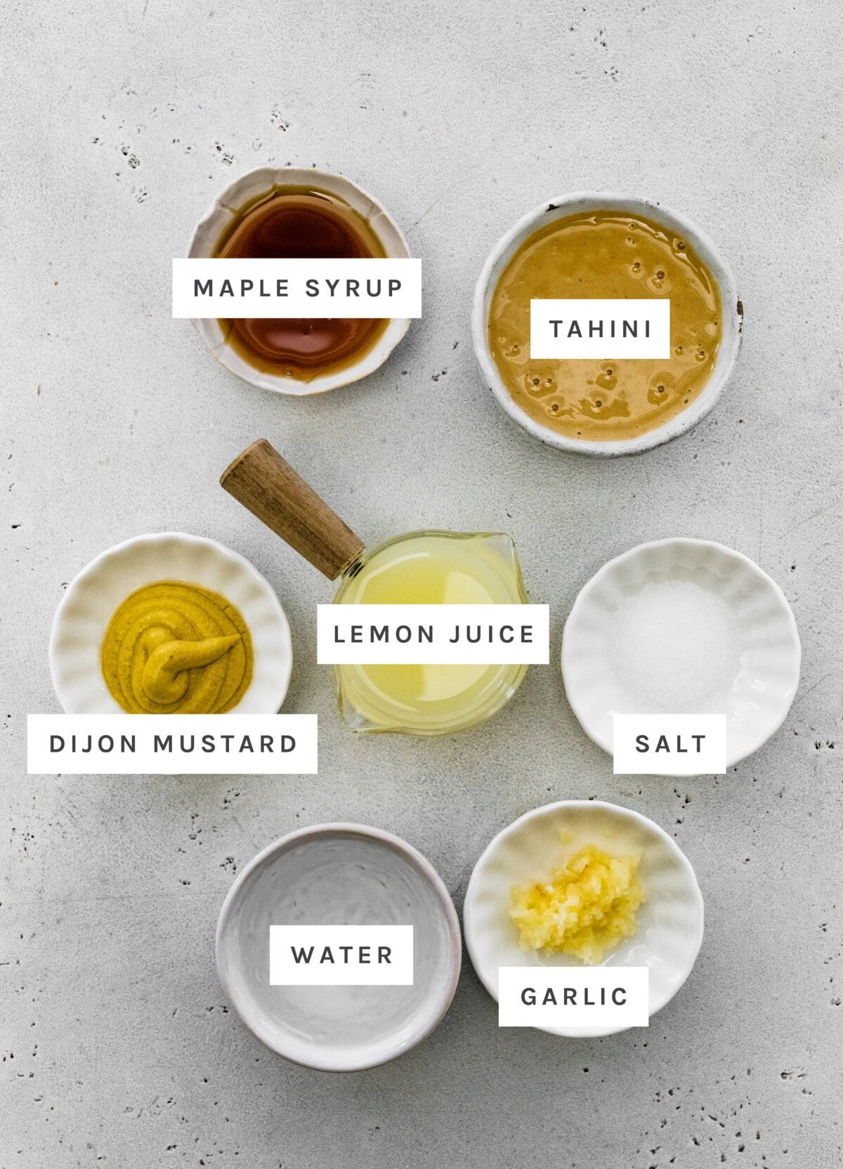 Ingredients measured out to make Tahini Dressing: Maple syrup, tahini, Dijon mustard, lemon juice, salt, water, and garlic.