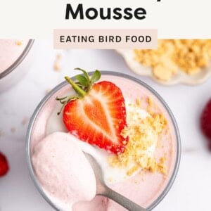 Glass of high-protein strawberry mousse topped with yogurt, crushed cookies, and a fresh strawberry half, with a spoonful scooped out.