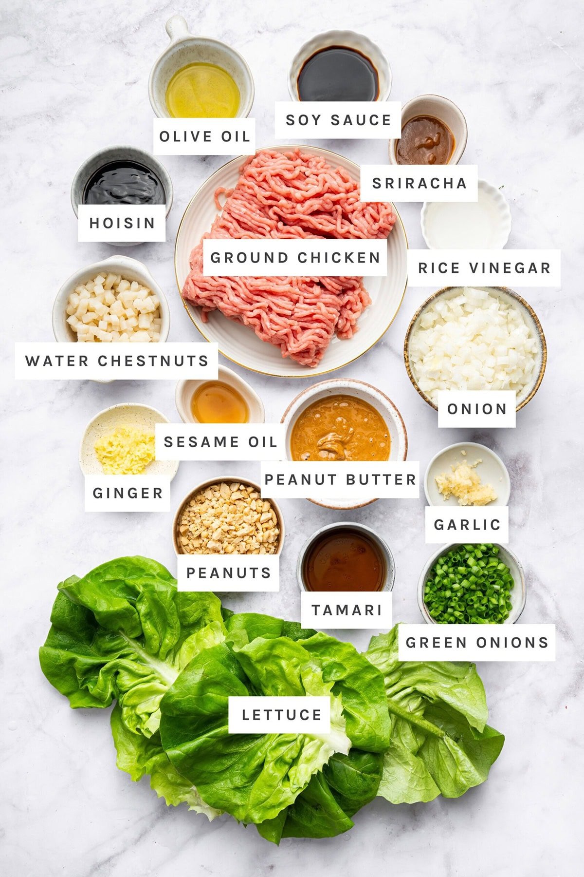 Ingredients measured out to make Asian Chicken Lettuce Wraps: Olive oil, soy sauce, sriracha, hoisin, ground chicken, rice vinegar, water chestnuts, onion, sesame oil, peanut butter, ginger, garlic, peanuts, tamari, green onions, lettuce.