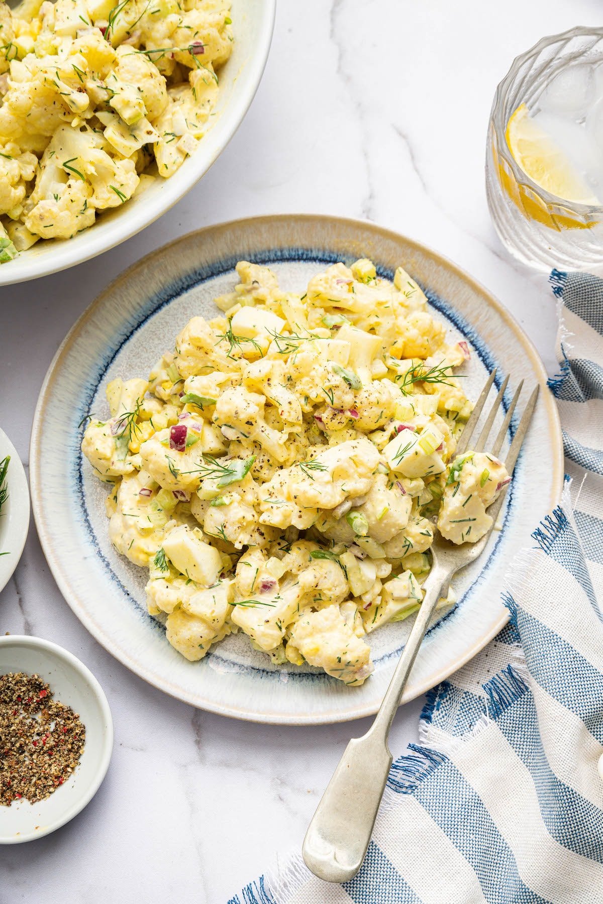 Cauliflower potato salad served on a plate with a silver fork. The salad is topped with fresh dill.
