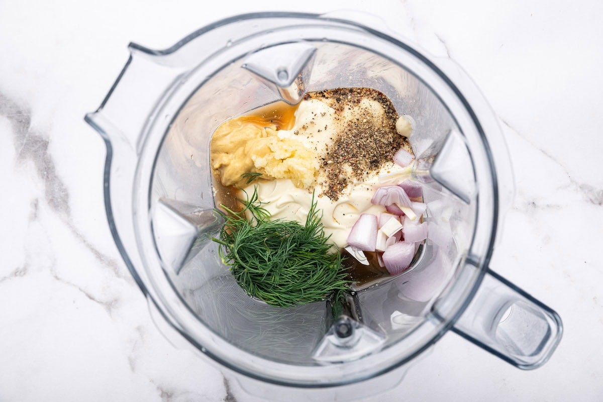 Ingredients for the creamy mayo dressing in the base of a blender: fresh dill, mayo, shallot, garlic, apple cider vinegar, mustard, salt and pepper.