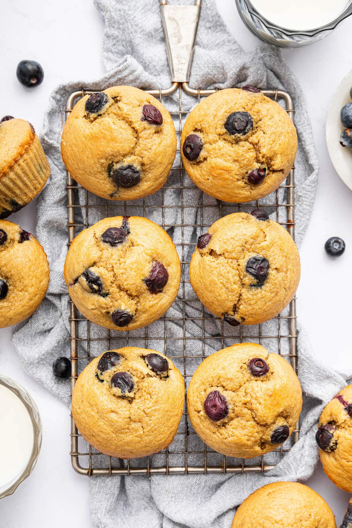 Six cottage cheese blueberry muffins on a wire cooling rack with more muffins next to it.