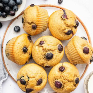 Seven cottage cheese blueberry muffins on a plate. Three of the muffins are on their side.