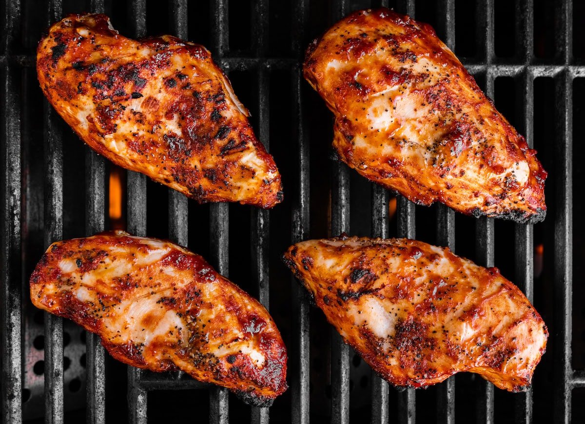 Four grilled BBQ chicken breasts on a grill.