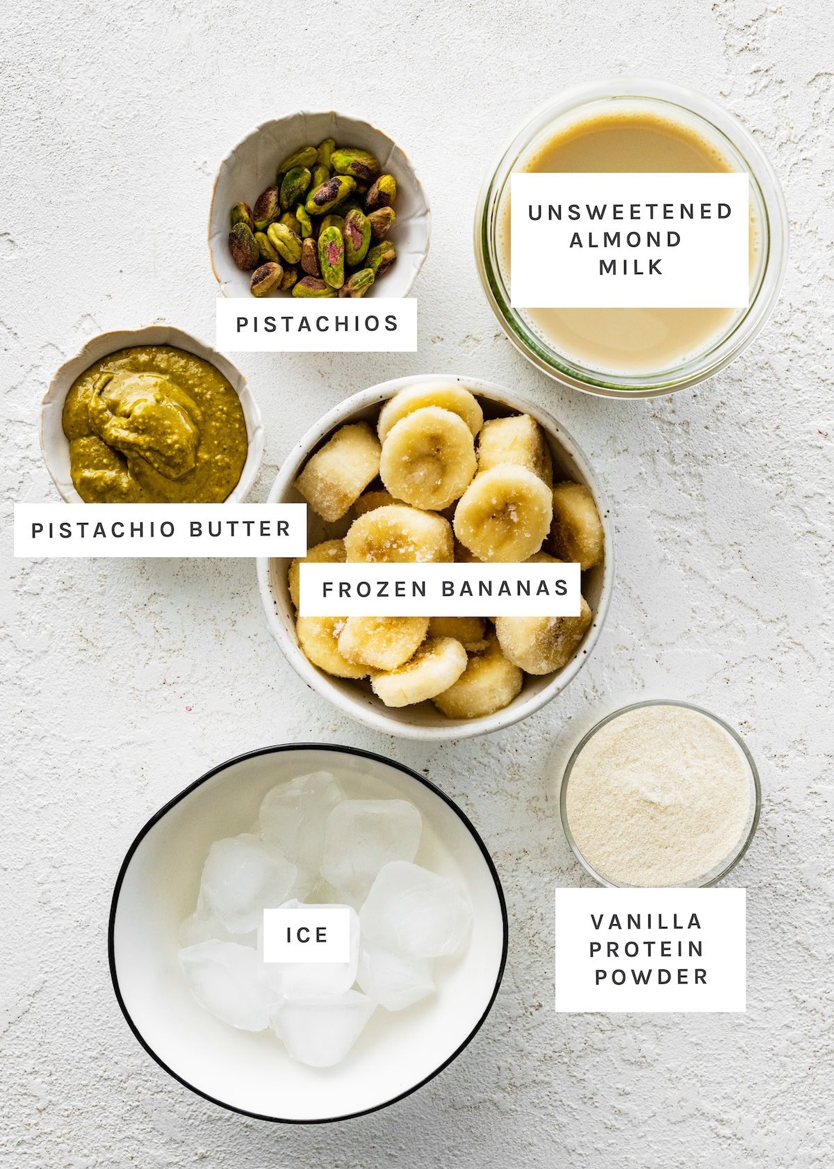 Ingredients for the pistachio protein smoothie: frozen bananas, almond milk, pistachios, vanilla protein powder, ice and pistachio butter.