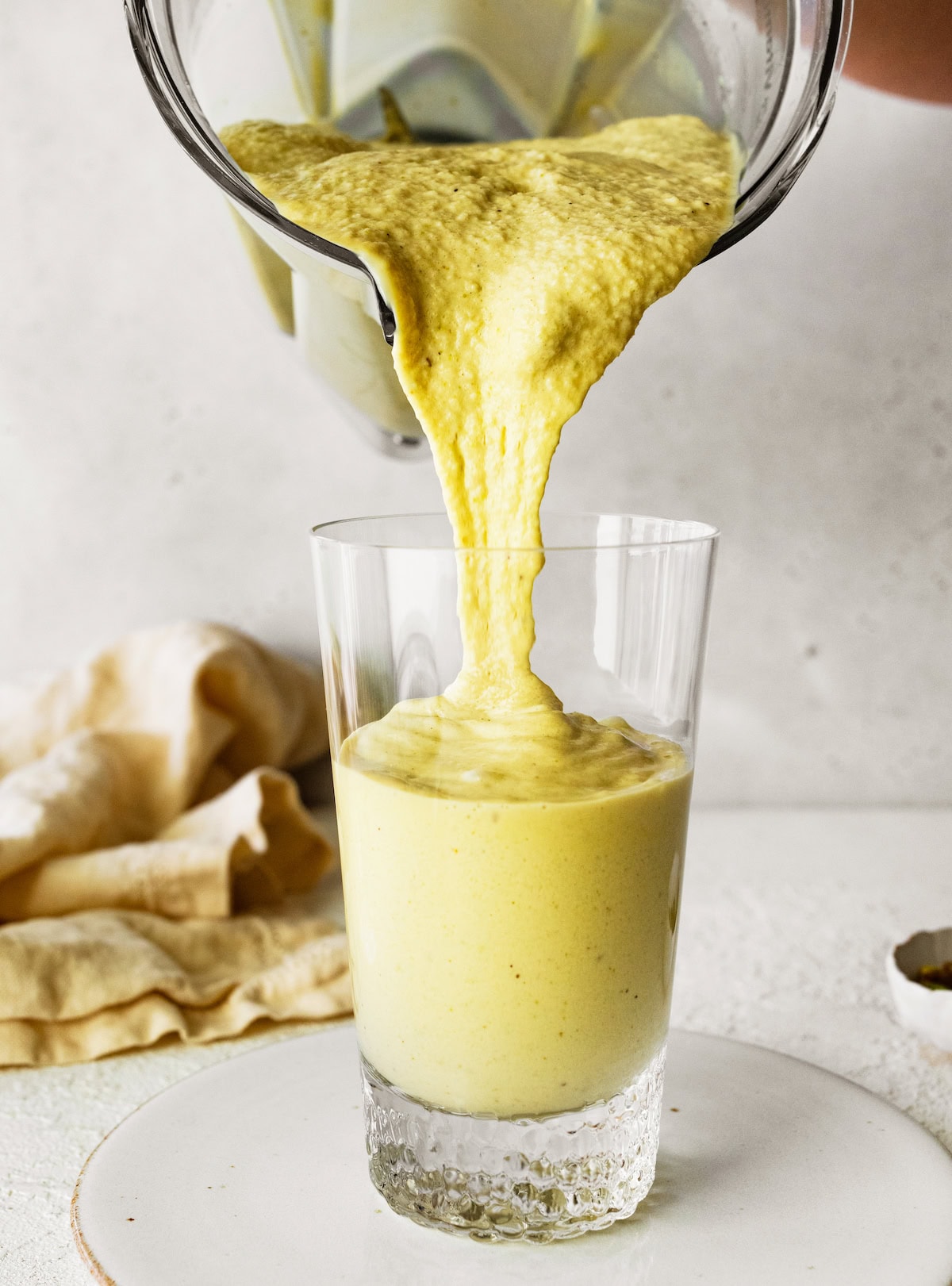 The pistachio protein smoothie being poured into a glass from the base of a blender.