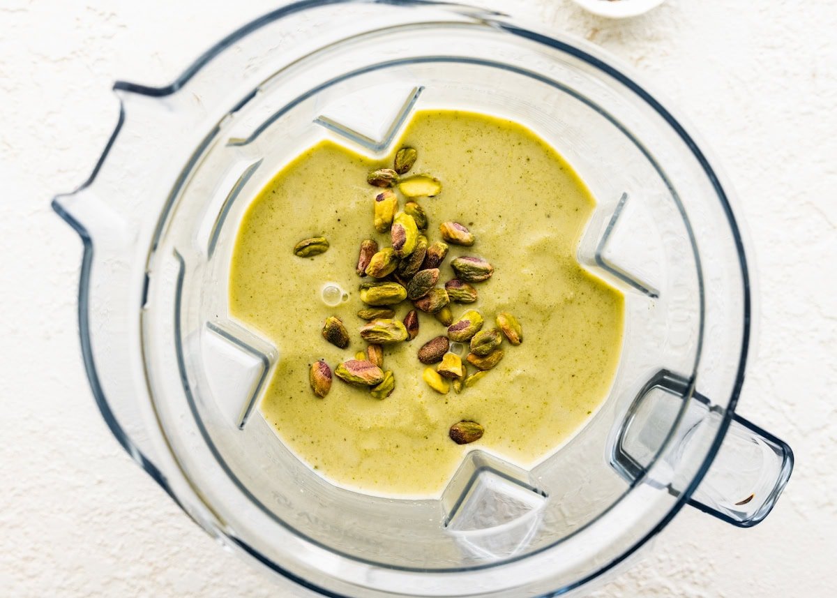 The blended pistachio smoothie in the base of a blender with unshelled pistachios tossed in.