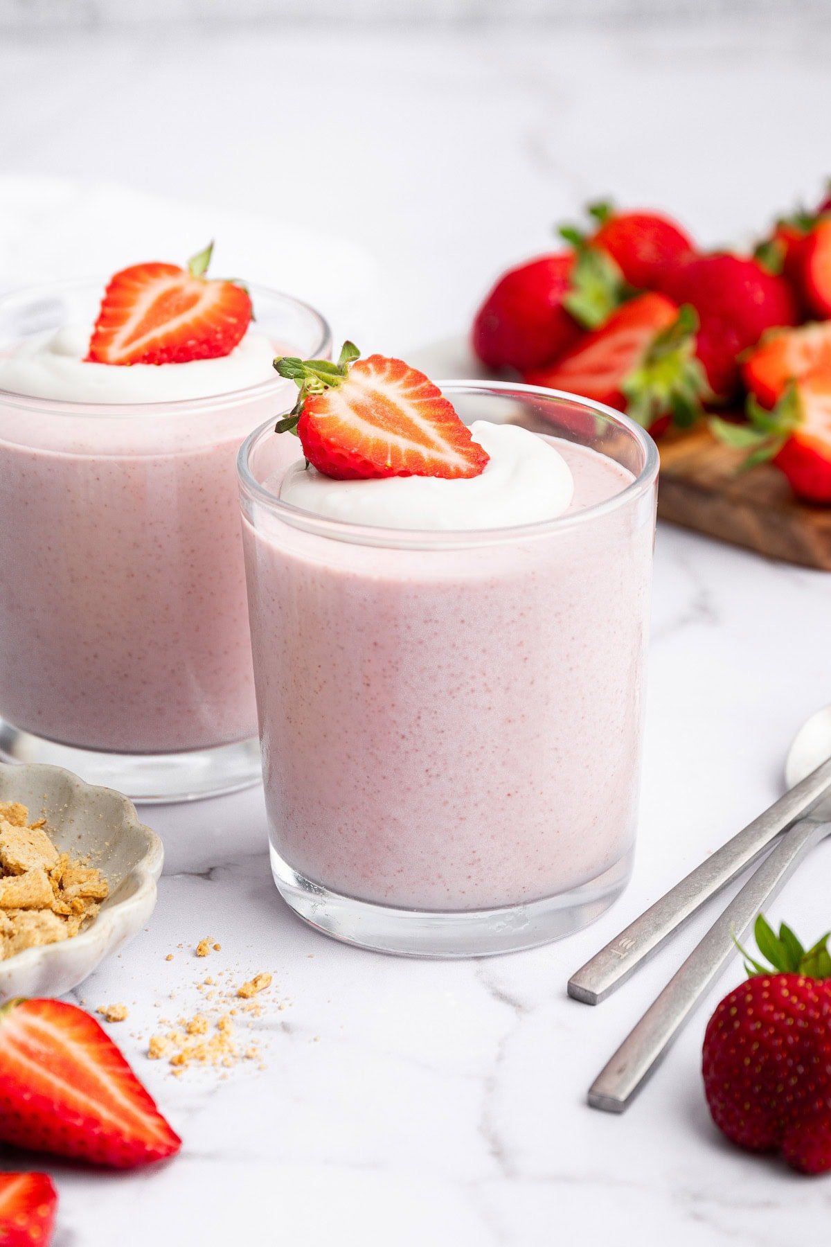 Two glasses filled with high-protein strawberry mousse topped with a dollop of cocowhip and a halved fresh strawberry.