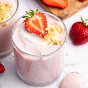 One glass filled with high-protein strawberry mousse topped with a dollop of cocowhip, one halved fresh strawberry and crushed graham crackers.