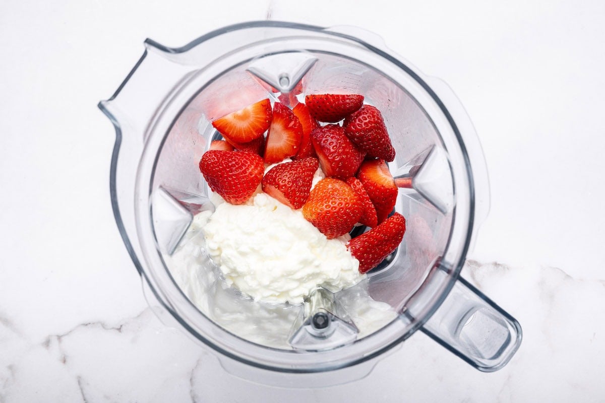 Fresh strawberry slices and cottage cheese in the base of a blender.