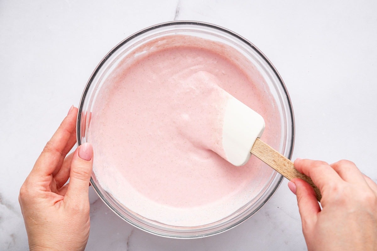 A woman's hand mixing the cocowhip into the strawberry cottage cheese mixture with a spatula.