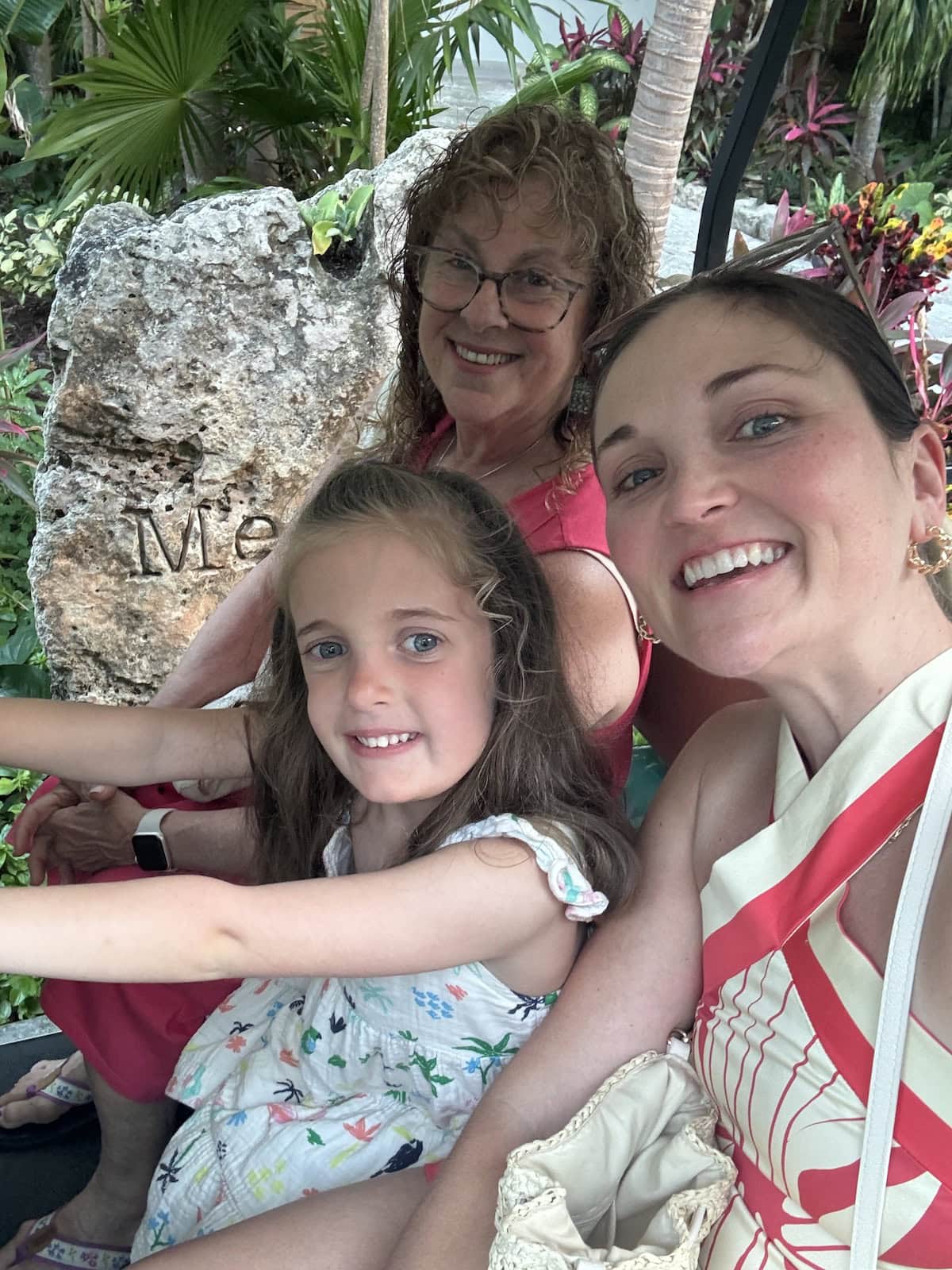 A grandmother, mom, and daughter smiling while riding a golf cart through lush greenery.