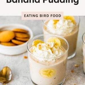 High protein banana pudding in glass cups, topped with whipped cream and banana slices, with vanilla wafer cookies on the side.