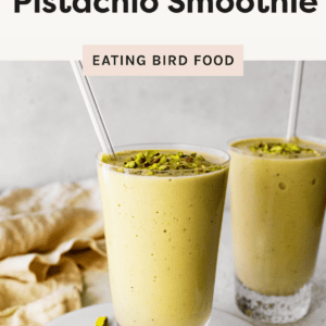 Two glasses of healthy pistachio protein smoothie topped with chopped pistachios, served with glass straws on a light background.