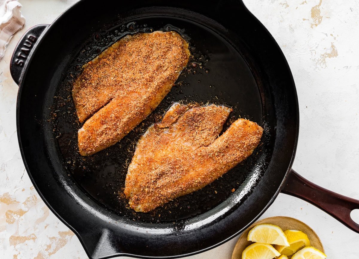 Two tilapia filets cooking in a cast iron skillet.