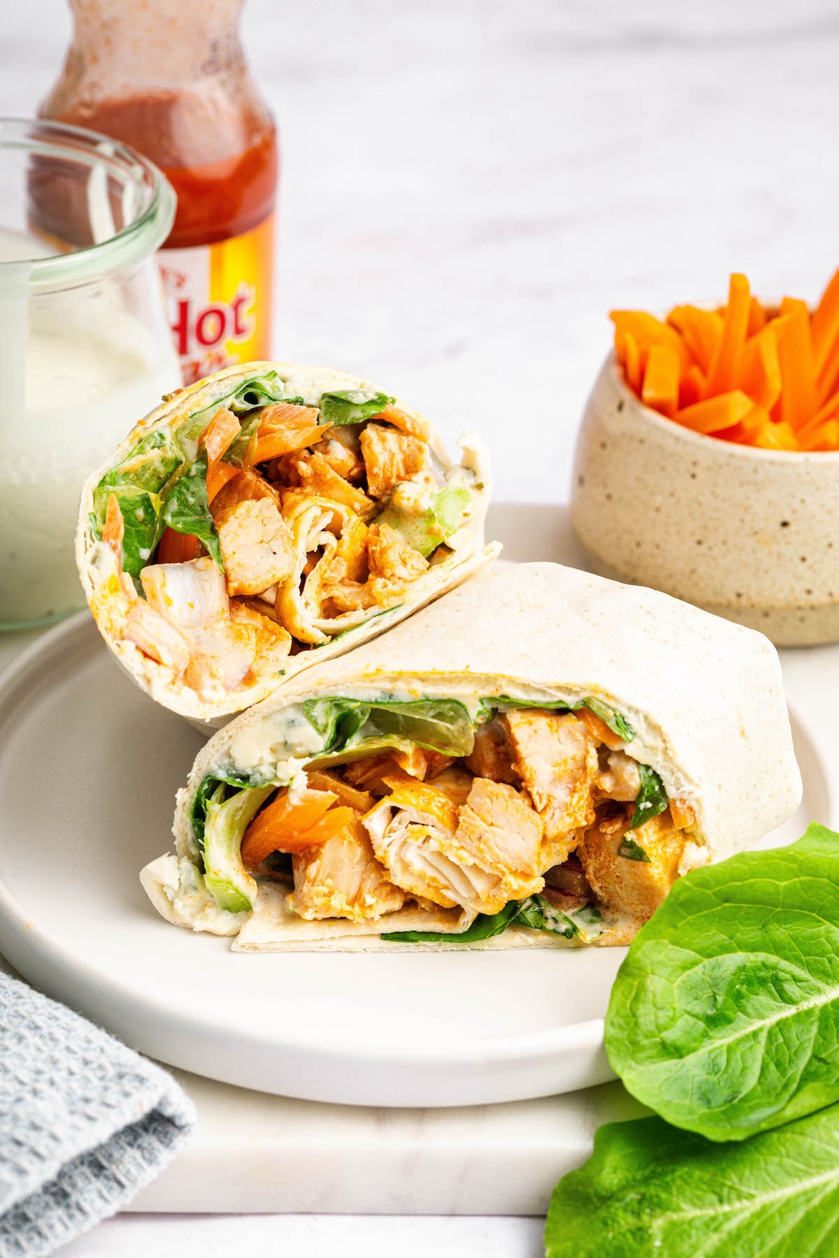 Buffalo chicken wrap cut in half and stacked on a plate with crisp lettuce and creamy dressing.
