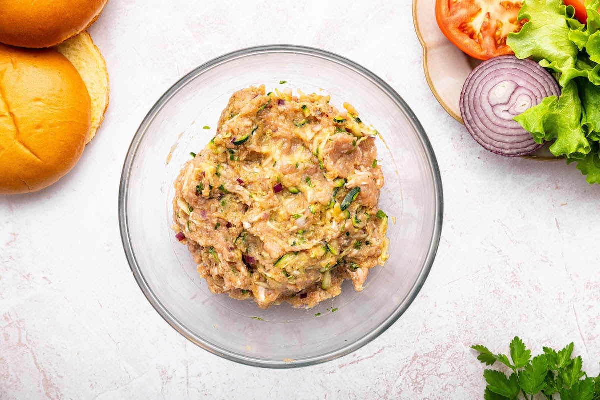 The combined ground chicken mixture for the chicken burgers in a glass bowl.