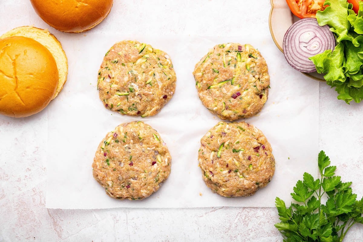 Four raw ground chicken burger patties formed on parchment paper.